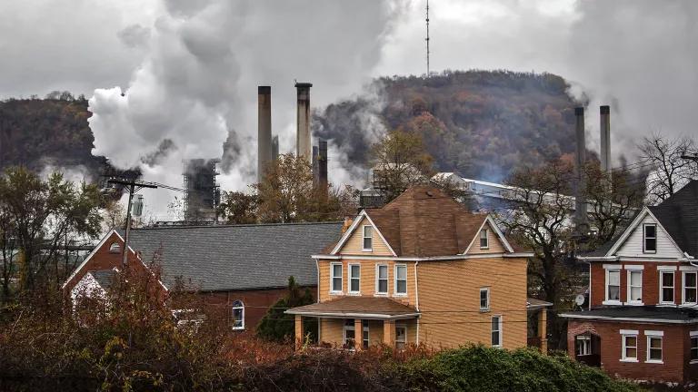 A row of houses with industrial smokestacks and plumes of emissions in the background