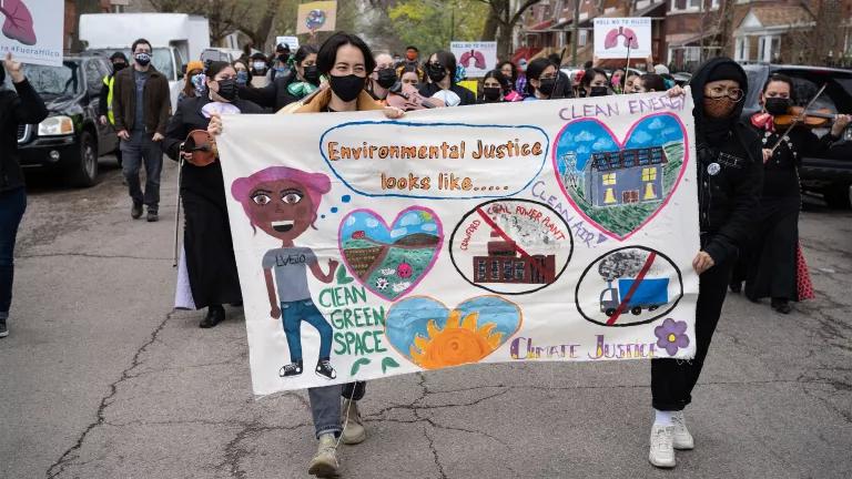 A large group of environmental organizers marching through a residential Chicago neighborhood, holding a sign that reads “environmental justice looks like, clean green space, clean air, clean energy and climate justice”