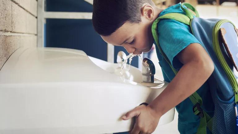 A young student drinking from a school water fountain.