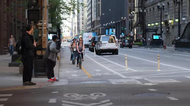 Cyclists using a protected bike lane as pedestrians wait to cross a street in downtown Chicago