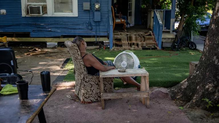 Woman sitting outside a house with a large fan