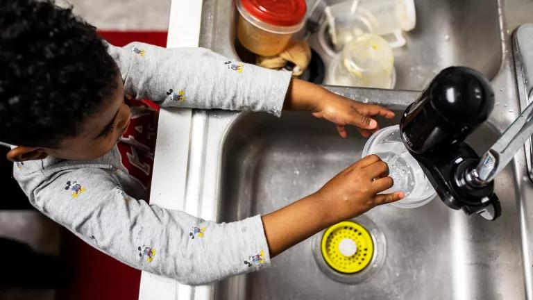 A boy fills a cup with water from the kitchen faucet in his Newark home.