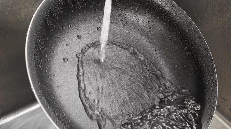 A non-stick frying pan being rinsed in a kitchen sink.