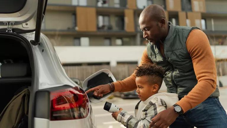 A father showing his son how to charge a white electric vehicle