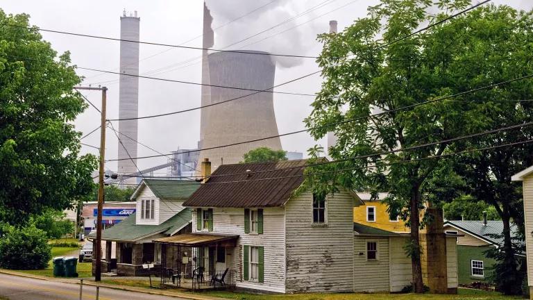 Homes lined on a street with large power plants right behind them, spewing out pollution