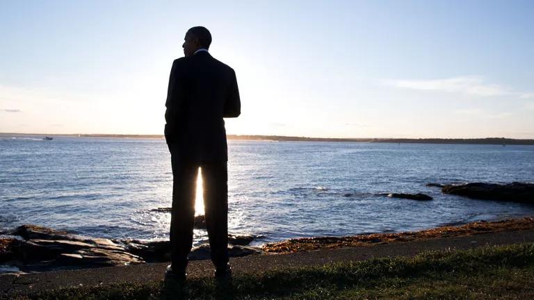 President Barack Obama stands on a beach and looks out over water