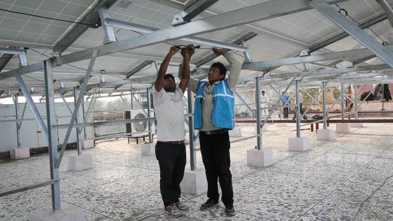 Two men reach up to work on a metal structure on the roof of a building