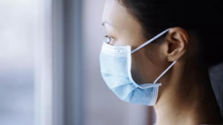 A woman wearing a protective face mask as she looks out a window.