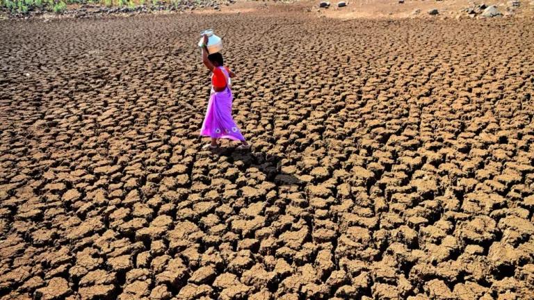 A woman carries a jug of water across parched land