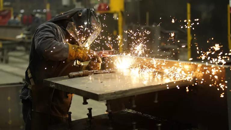 A worker in protective gear welds a steel beam as sparks fly