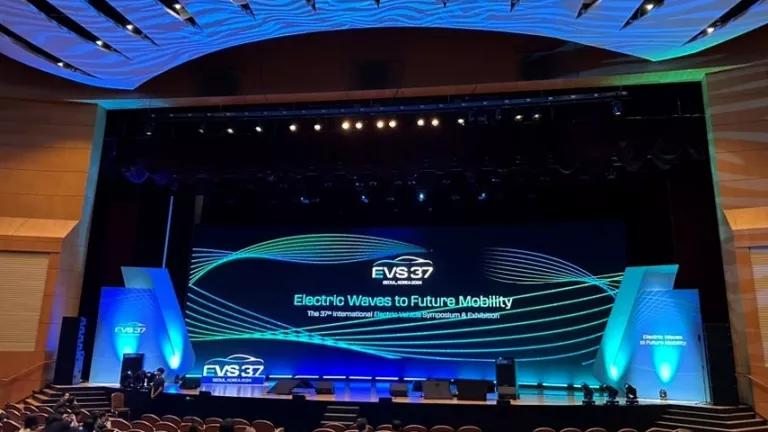 An auditorium stage lit up with a backdrop and the words "Electric Wave to Future Mobility"