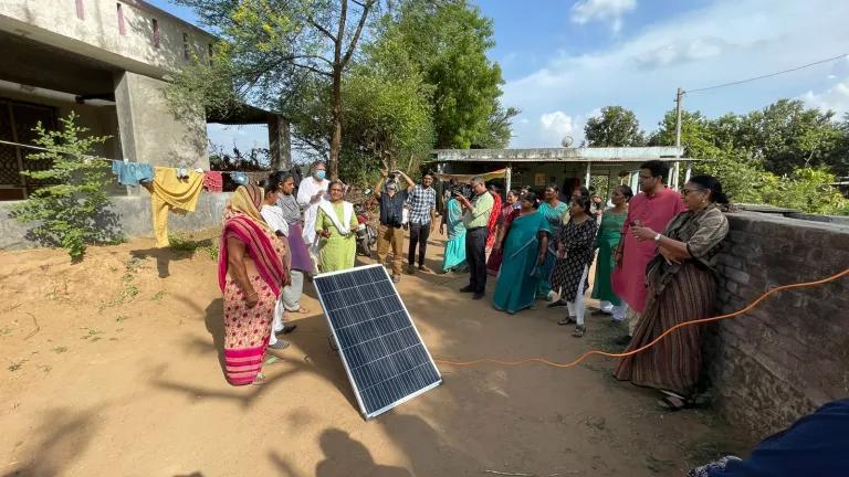 A group of people standing around a solar panel that's propped up with a stick