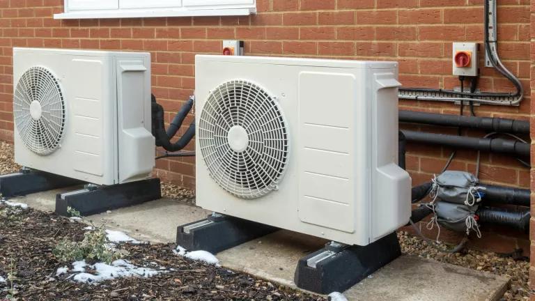 Two heat pump units outdoors in front of a brick building
