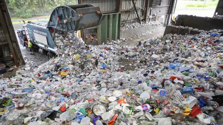 A truck dumps its contents of recyclable plastic items onto a mound of plastic in a warehouse.