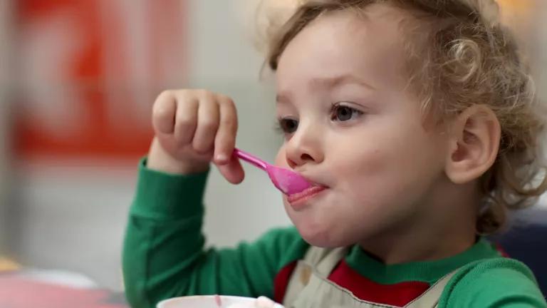 A toddler eats ice cream using a plastic spoon.