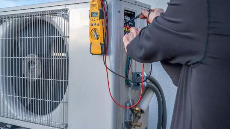 A technician using a multimeter to test voltage on a mini-split heating and cooling system.