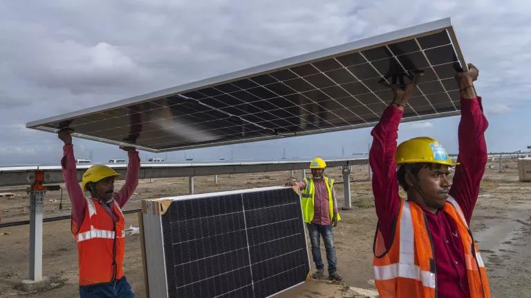 Workers carry a solar panel at the under-construction Adani Green Energy Limited's Renewable Energy Park in the salt desert of Karim Shahi village, Gujarat, India, on September 21, 2023.