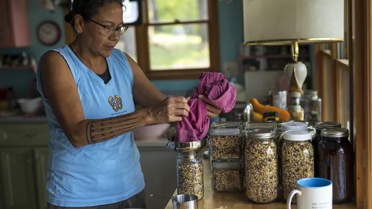 A woman pours seeds into a glass jar on a kitchen counter
