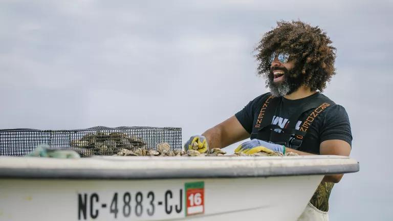 A man stands next to a small boat and handles oysters