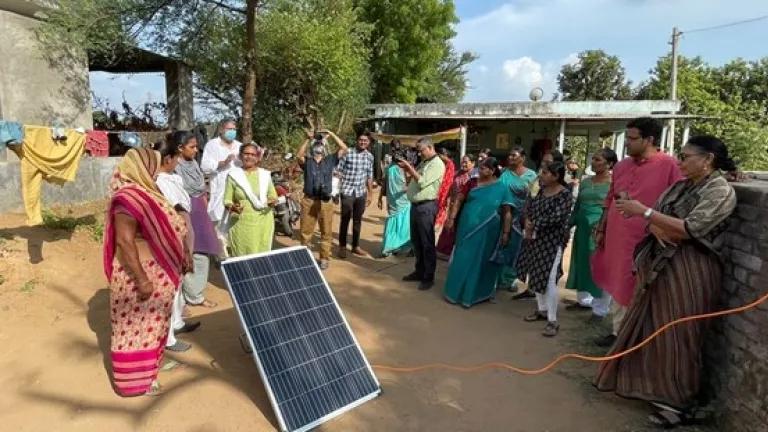 women in India stand around a solar panel discussing clean energy solutions