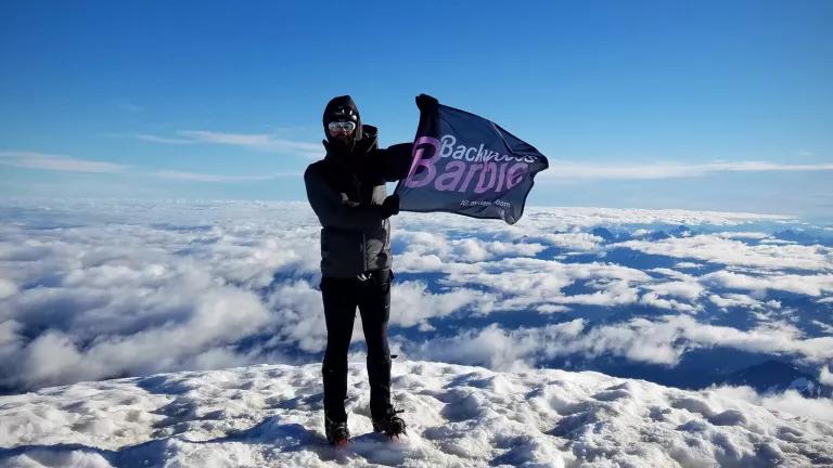 A person stands on the top of a snowy mountain peak above the clouds
