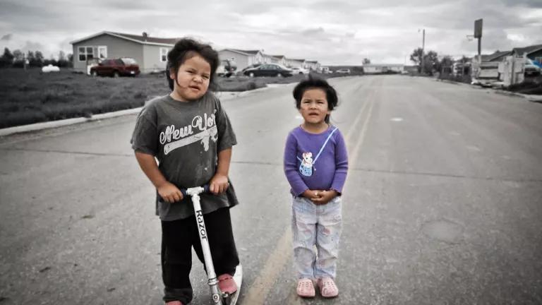 A photo of two Indigenous children standing in the middle of an otherwise-empty street, one holding a Razor scooter