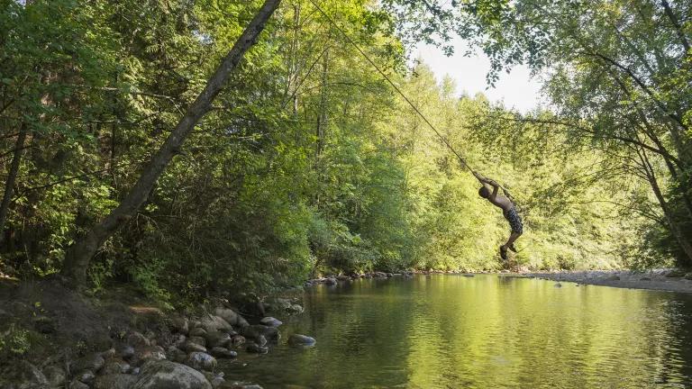 child playing on a rope swing over a river 