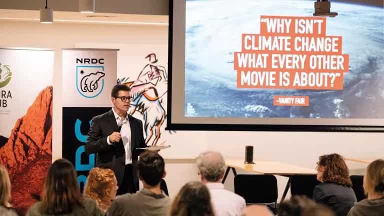 Daniel Hinerfeld delivering a presentation while standing in front of a slideshow that reads, "Why isn't climate change what every other movie is about?"