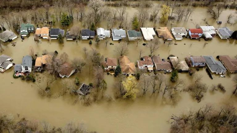 An aerial view of two rows of single-family homes that are completely surrounded by brown floodwaters.