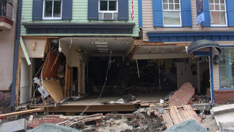The ground floor of a building is completely gutted and the front wall is missing, with debris lying on the street in front of it.