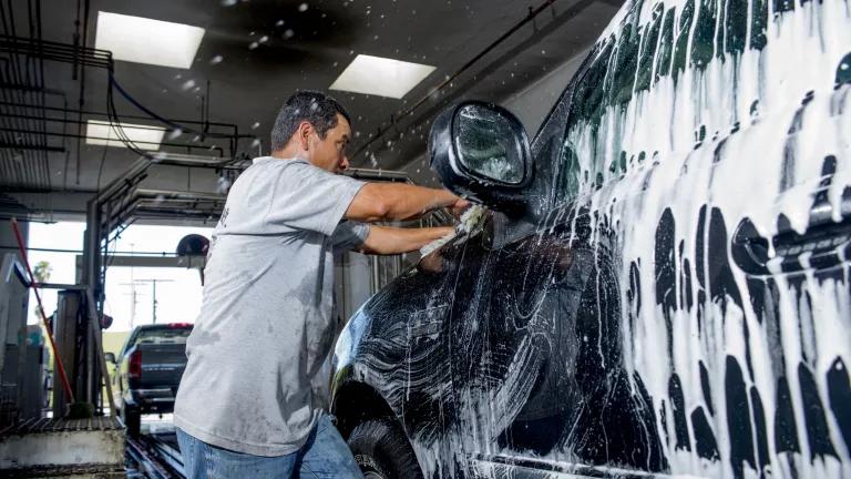Man in a gray tshirt scrubbing a black SUV
