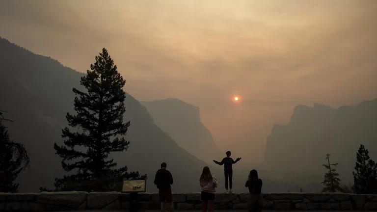 The sun and distant mountains are obscured by smoke as people look on