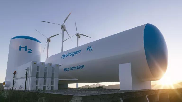 A larger tank with the word "hydrogen" on it sits in front of three wind turbines