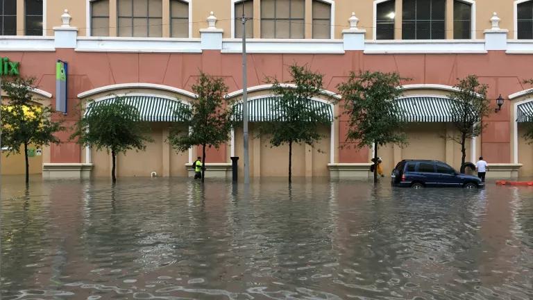 People walk through floodwaters up to their knees in front of a commercial building. 