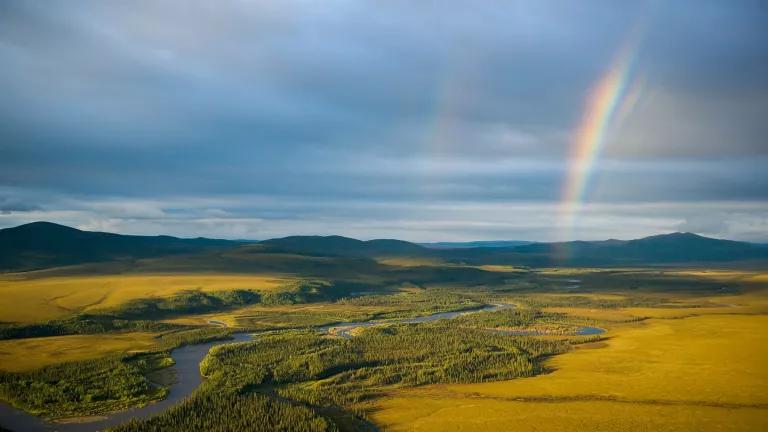 A rainbow touches the horizon over an expanse of forested and grassy land