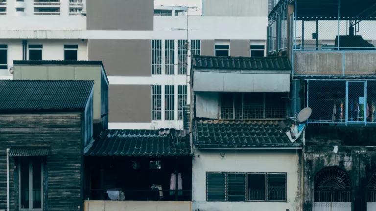 The image captures a moment showcasing the juxtaposition of aging, traditional urban buildings and a modern, high-rise structure in a dense city landscape. 