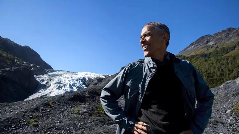 President Barack Obama looks out over rocky clearing with snowy and grassy mountains behind him