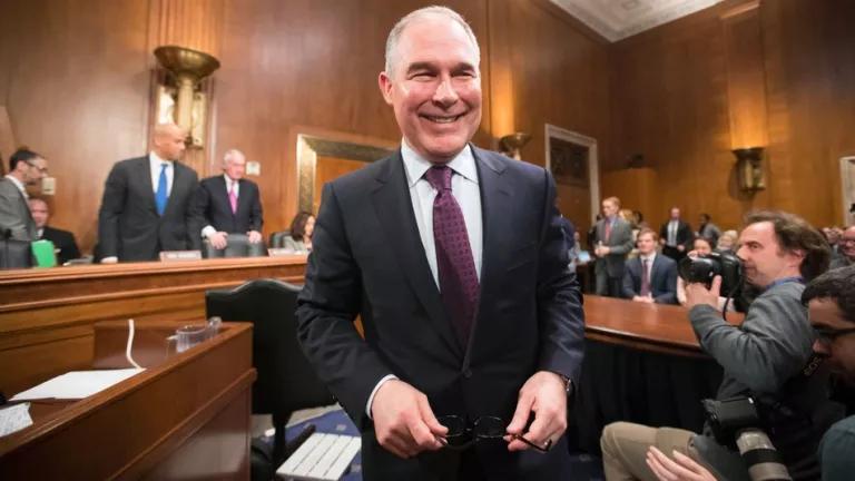 Scott Pruitt stands smiling in a crowded wood-paneled room