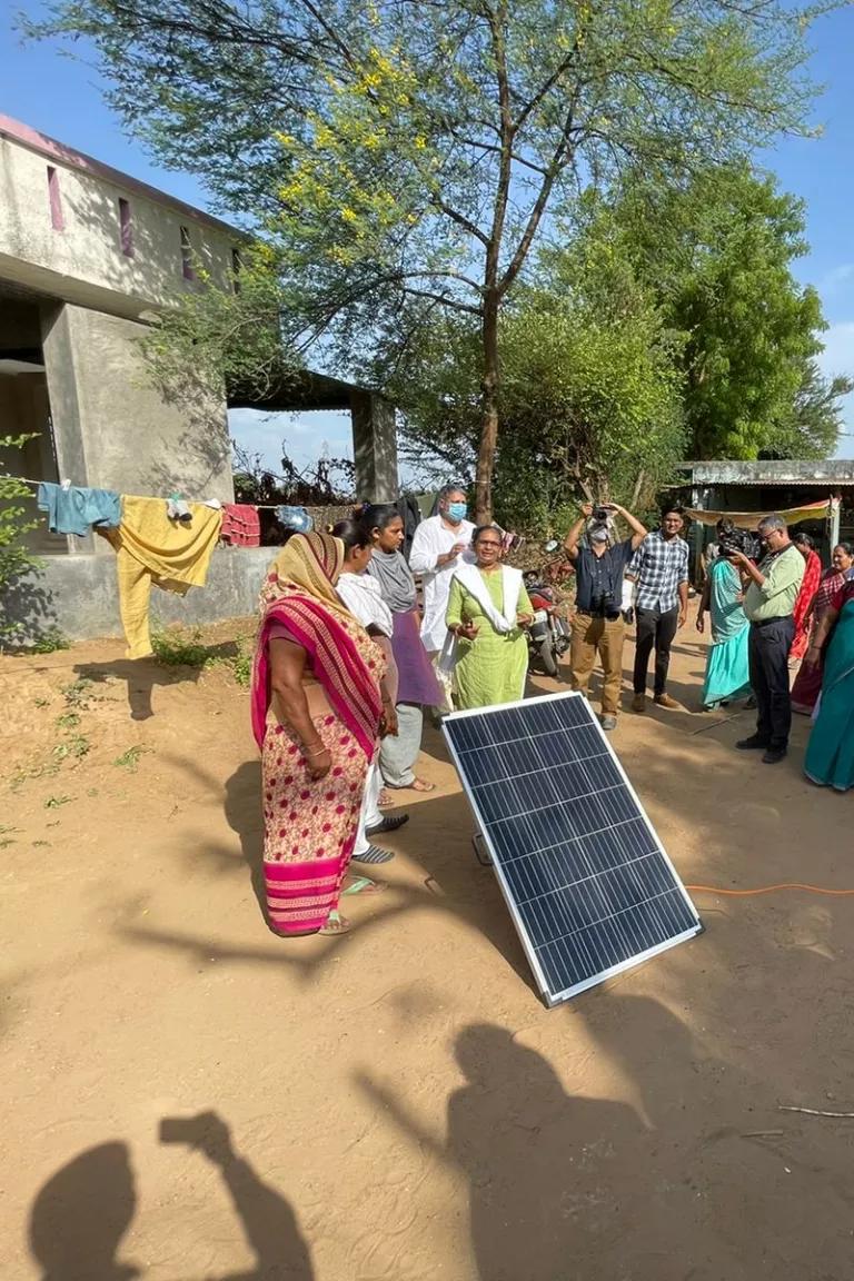A group of people standing around a solar panel that's propped up with a stick