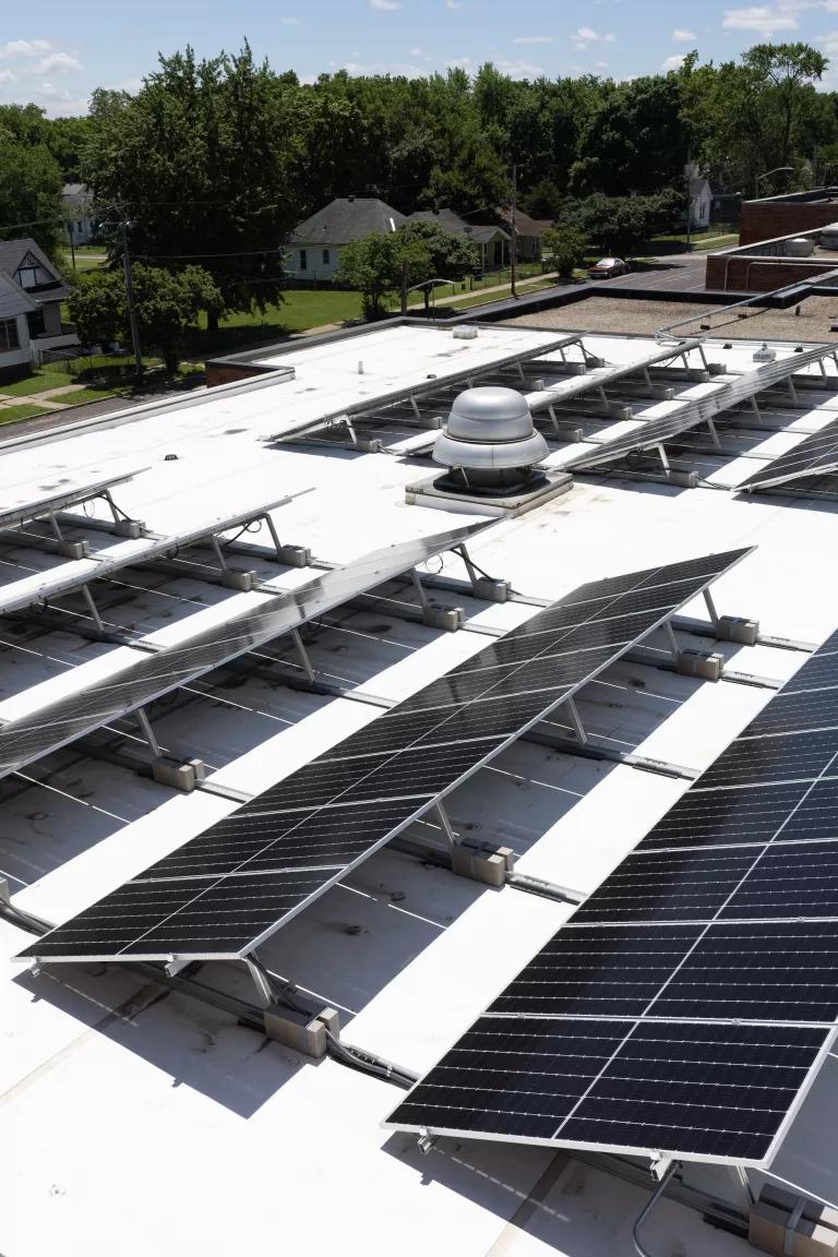An array of solar panels with homes and a red brick building in the background