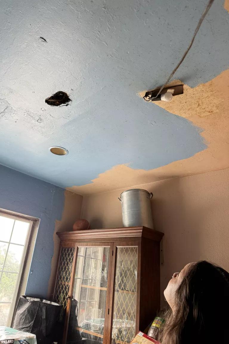 Valdovinos looks up at holes and exposed wires in the ceiling of her family home in Oakland, California.