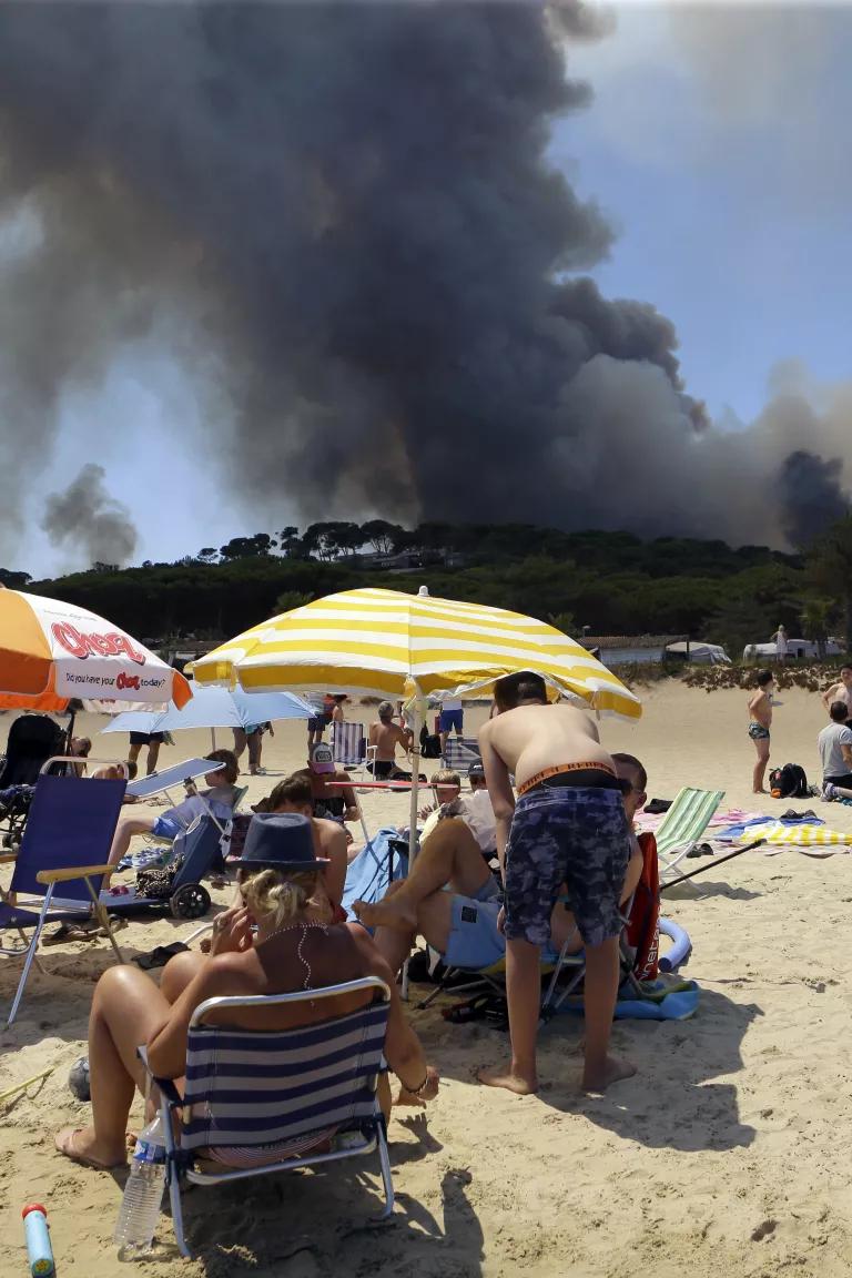 People sunbathing on the beach in Lavandou, French Riviera, as plumes of smoke rise in the air from burning wildfires in the forest of La Londe-les-Maures, France on Wednesday, July 26, 2017.