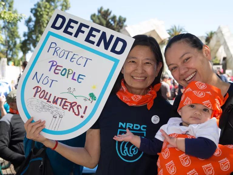 Two people at the Rise for Climate March, one with a sign that says "Protect People Not Polluters," the other one hold a baby