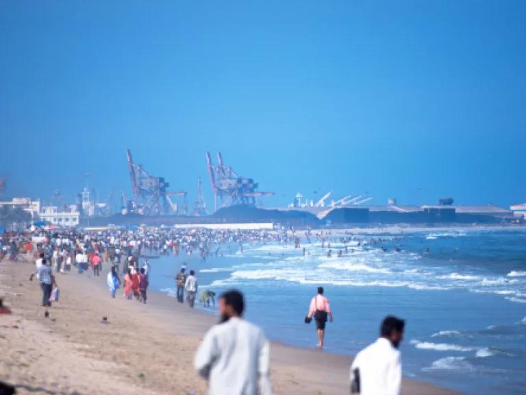 A crowded beach in Chennai, India, with coal and industry facilities in the background