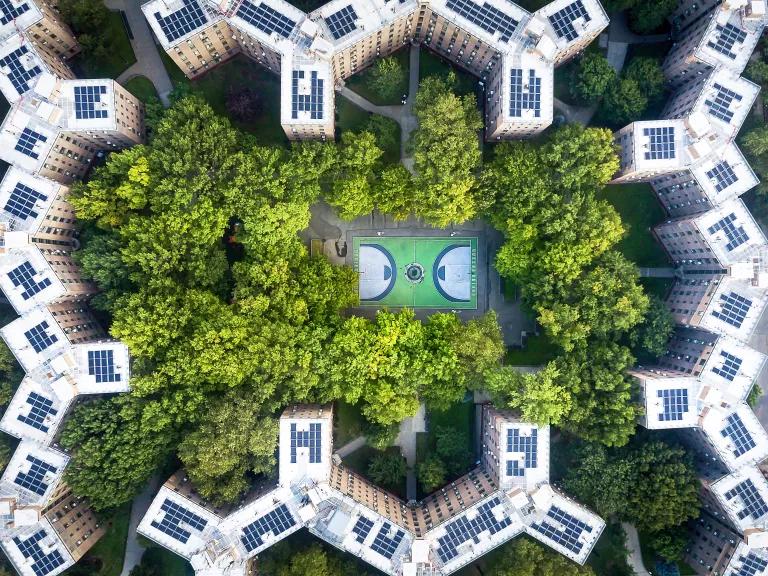 An aerial view of the Queens Bridge Houses basketball court surrounded by trees and solar rooftops in New York