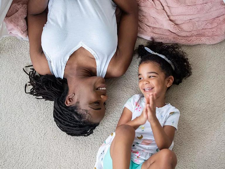 A mother and child lying on a carpeted floor in their home
