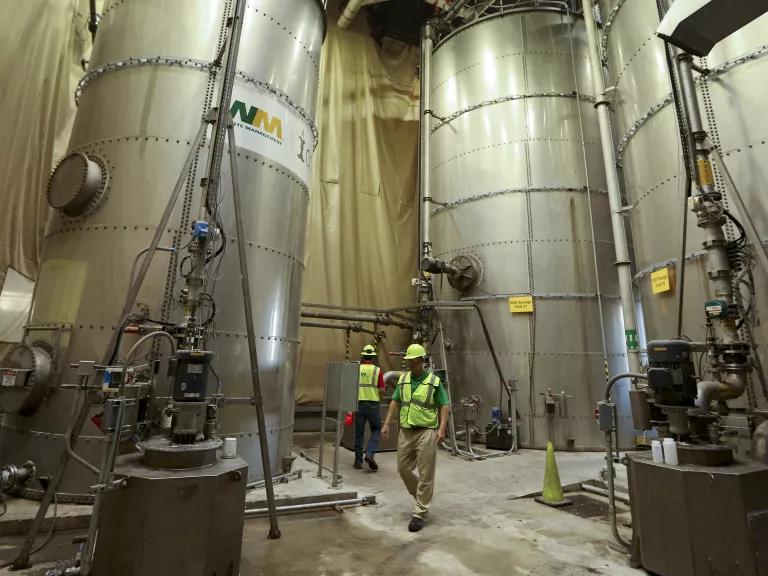 Two workers beside huge 'bio-slurry' production tanks at a Waste Management facility in New York City.