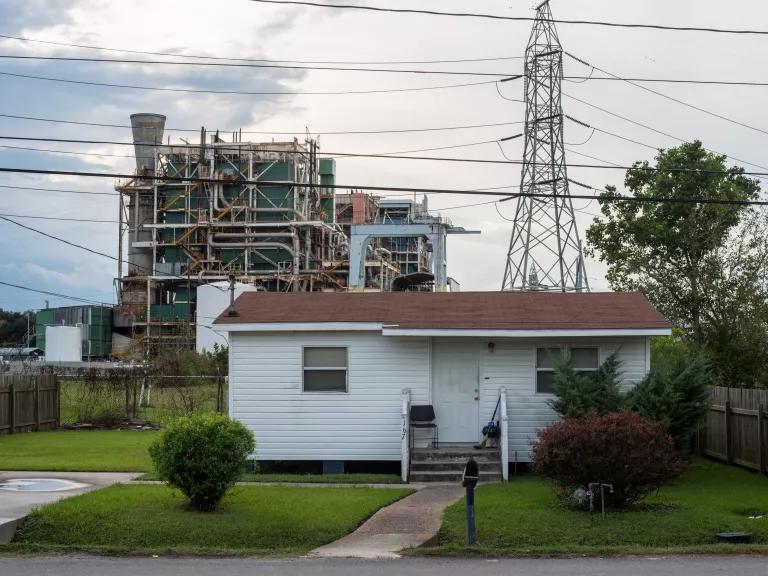 A house sits in the forefront of an electrical tower and a chemical plant.