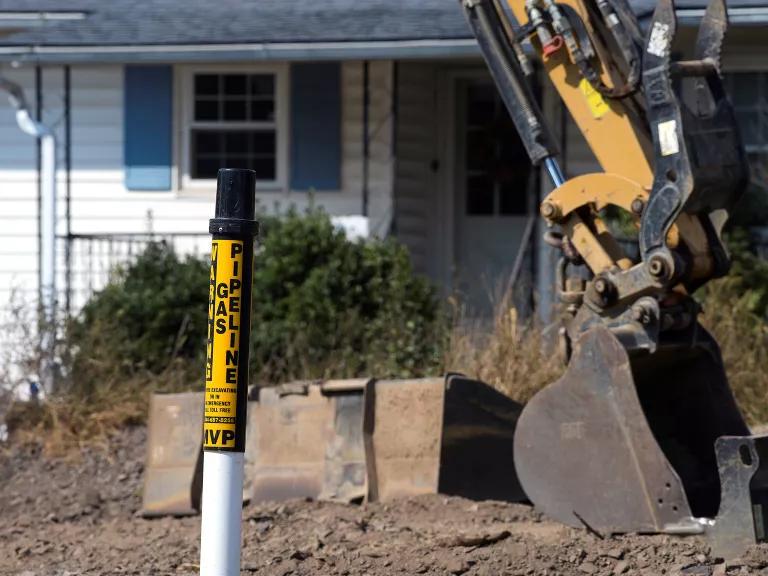 A warning sign and digger at a Mountain Valley Pipeline construction site near a home.