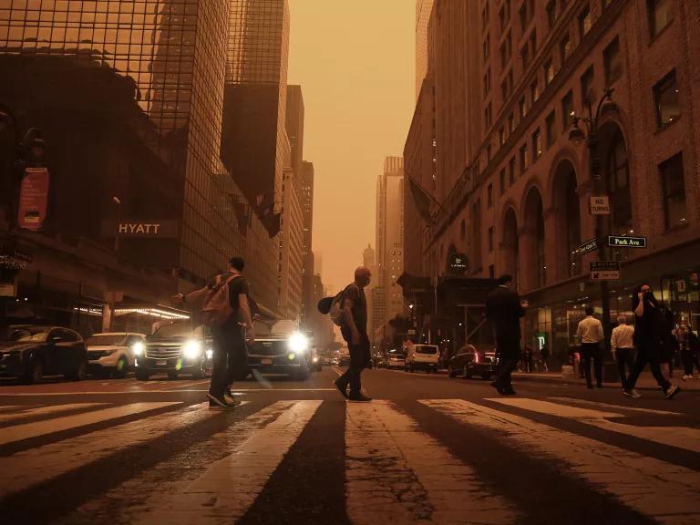 A busy Manhattan street is shadowed by a hazy orange sky